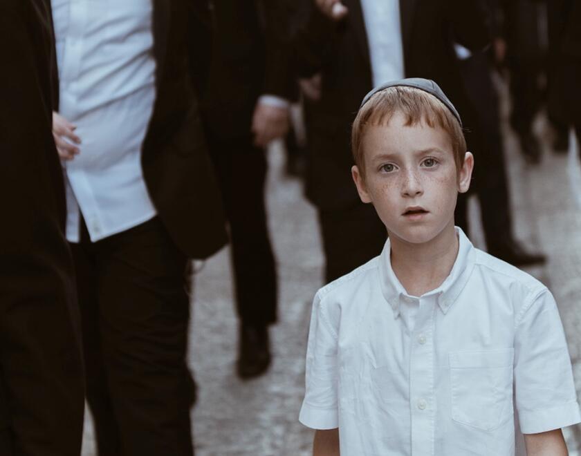 A Jewish child walks among Jewish men